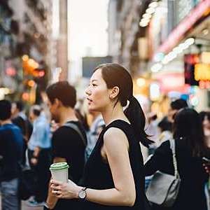 Young woman with coffee standing in the crowd on busy downtown city street