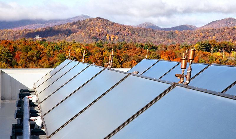 Rooftop view of solar panels against a colourful autumn landscape.