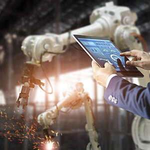 Manager industrial engineer using a tablet to control welding robot arms machine. 