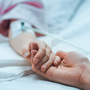Close up on the holding hands of a mother and her recovering child, lying in a hospital bed. 