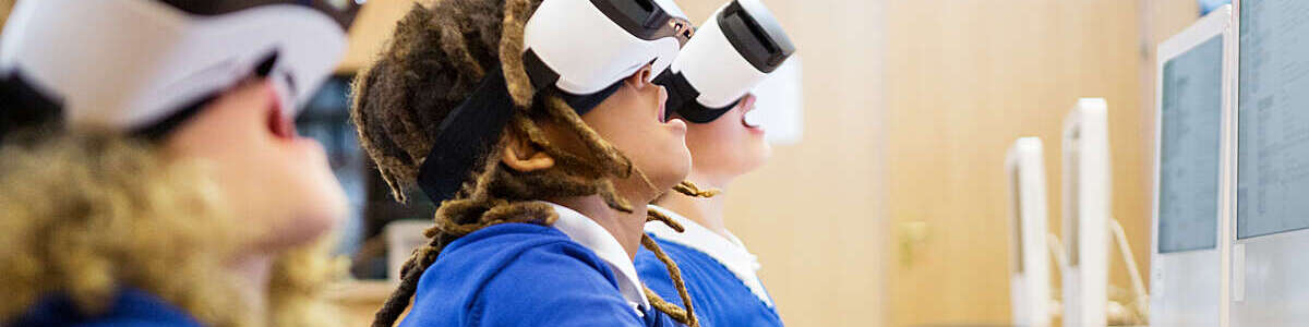 Young children, open-mouthed with excitement as they use virtual reality goggles in a computer lab at school.